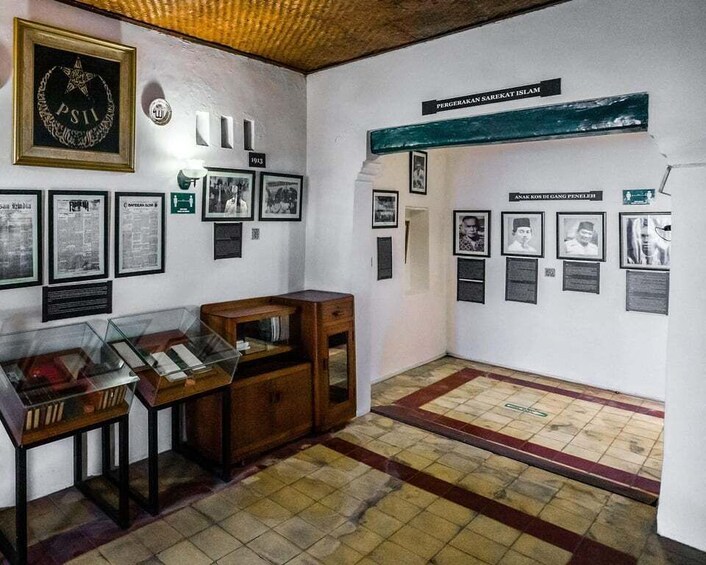A room with a display of historical documents and photographs, a wooden cabinet, and a tiled floor. 4