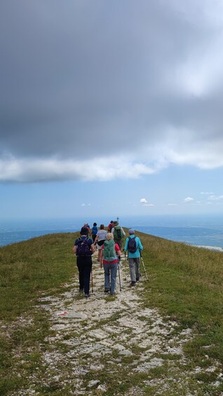 A group of hikers on a rocky path with a view of the ocean and cloudy sky. 3
