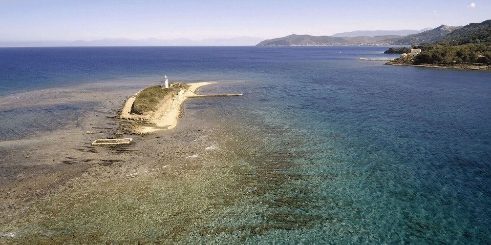 A coastal landscape with a lighthouse on a small island, clear blue waters, and distant hills. 4