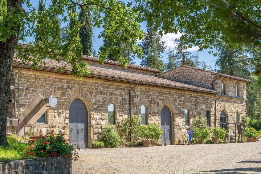 A stone building with arched windows and a tiled roof, surrounded by trees and potted plants. 2