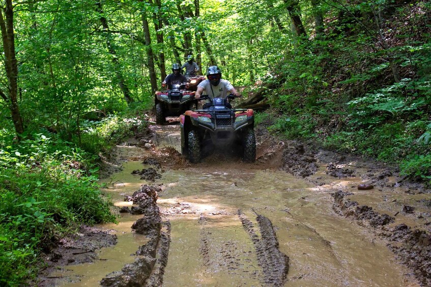 Two people riding ATVs on a muddy trail in a forest. 4