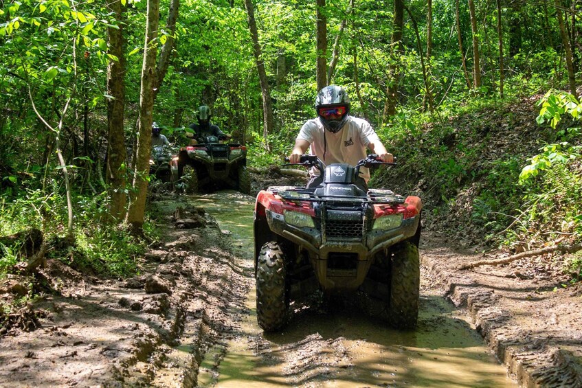 Two off-road vehicles navigating a muddy trail in a forested area. 3