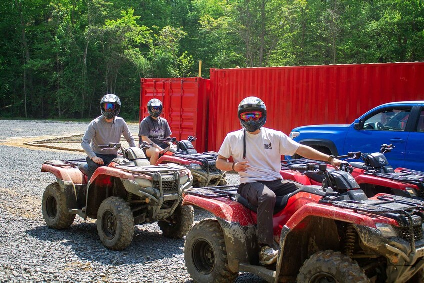 Three people on ATVs in front of a red container and a blue truck. 5