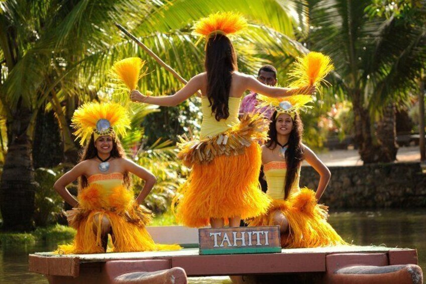 A group of people in vibrant yellow costumes with feathered headdresses, standing on a platform with a sign that reads 'TAHITI'. 2