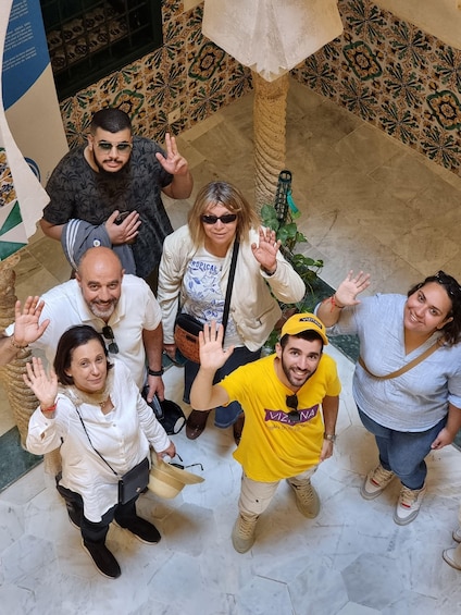 A group of people standing in a tiled courtyard with a patterned floor and a palm tree. 5