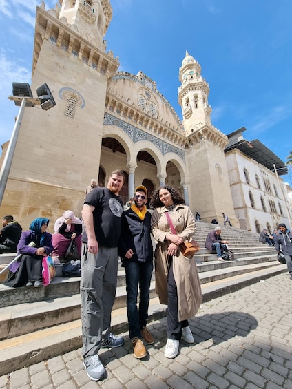 A group of people posing in front of a historic building with arches and a tower. 2