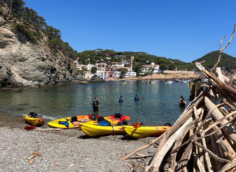 A rocky beach with kayaks, people in the water, and buildings in the background. 2