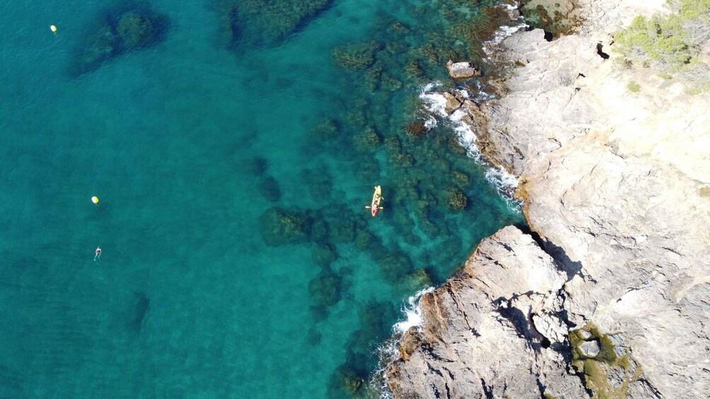 A coastal area with clear turquoise water, rocky shoreline, and a kayaker. 5