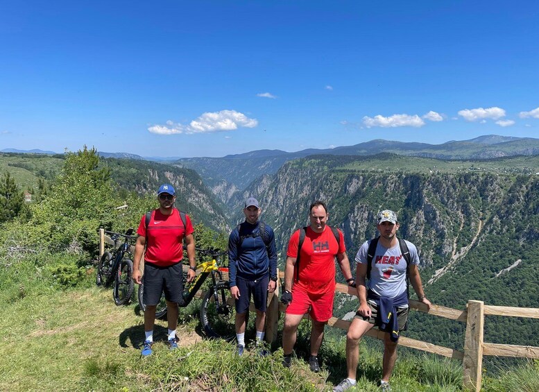 Four people standing on a grassy hill with a mountainous landscape in the background. 5