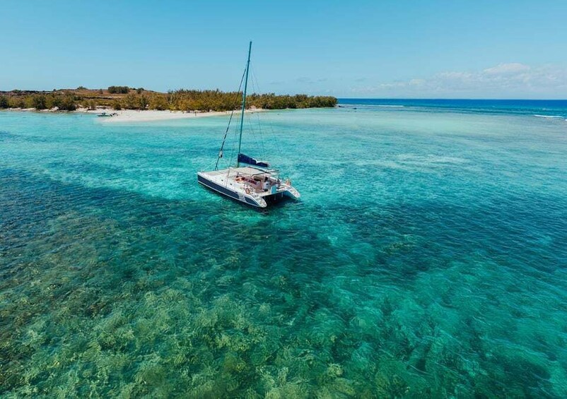 A sailboat on clear turquoise waters with a sandy beach and vegetation in the background. 1