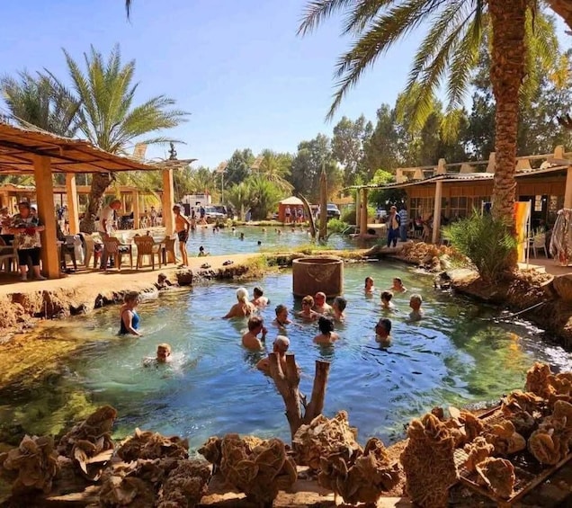 A natural hot spring with people swimming, surrounded by palm trees and wooden structures. 1
