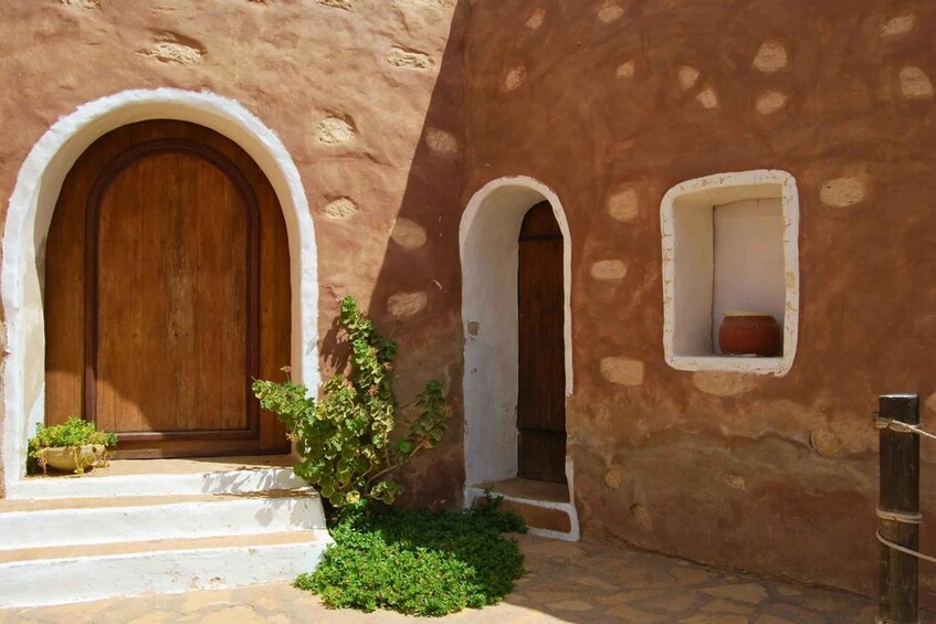 A building with arched wooden doors and windows, a small garden with plants, and a stone pathway. 2