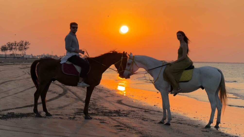 Two people riding horses on a beach at sunset. 4