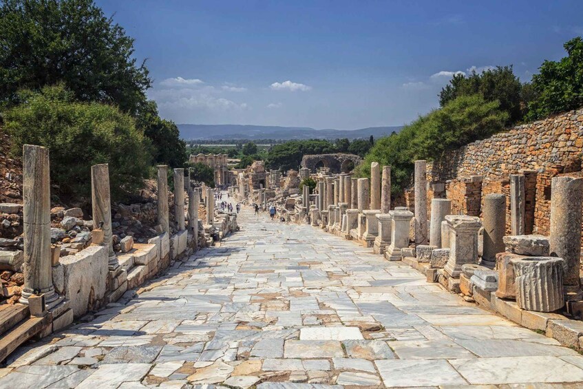 An ancient stone-paved pathway flanked by columns and ruins, leading towards distant hills. 5