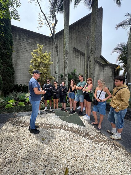A group of people standing in a garden with a stone wall and palm trees in the background. 2