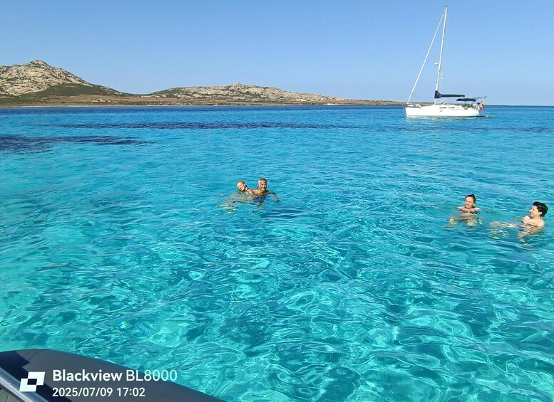 A clear blue sea with people swimming, a sailboat in the distance, and a rocky landscape in the background. 5