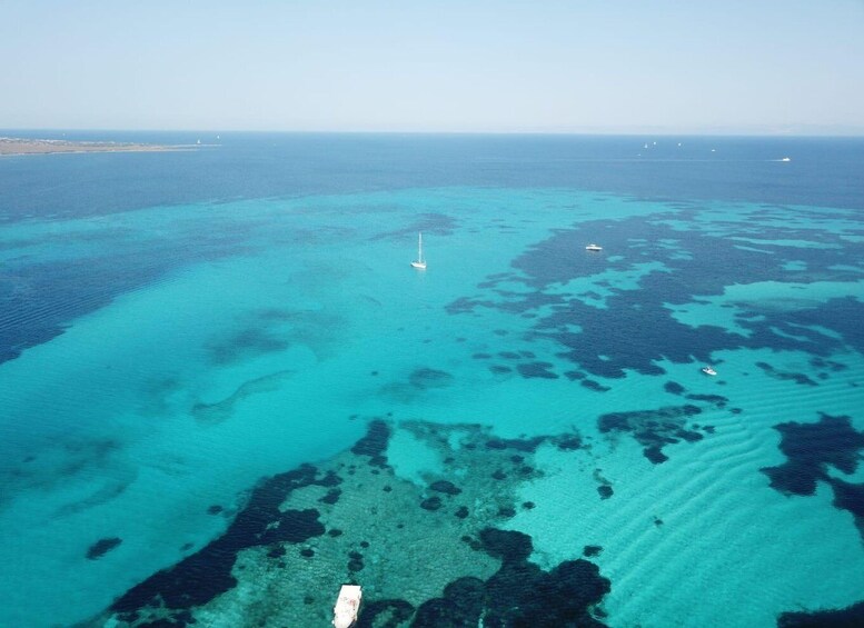 A clear blue sea with a sailboat and a small island in the distance. 2