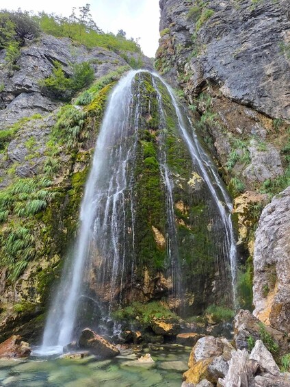A waterfall cascading down a rocky cliff surrounded by greenery. 2