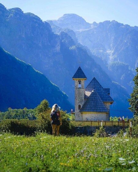 A small church with a bell tower and a person standing in front of it. 1