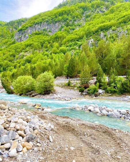 A river with clear water, surrounded by green trees and rocky terrain. 5