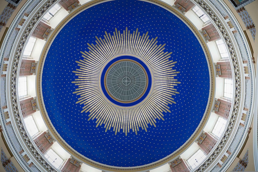 A large circular room with a blue ceiling and a golden sun-like design in the center. 5