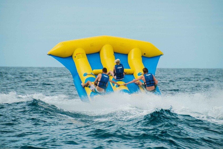 A group of people on a yellow and blue inflatable raft moving through the ocean. 2