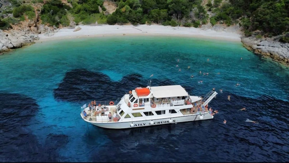 A boat named 'AILY CRUISER' on a turquoise sea with people swimming around it. 1