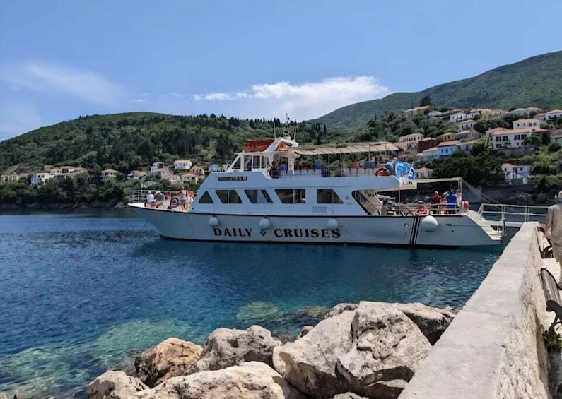 A white boat named 'DAILY CRUISES' docked at a pier with clear blue water and a hillside with houses in the background. 4