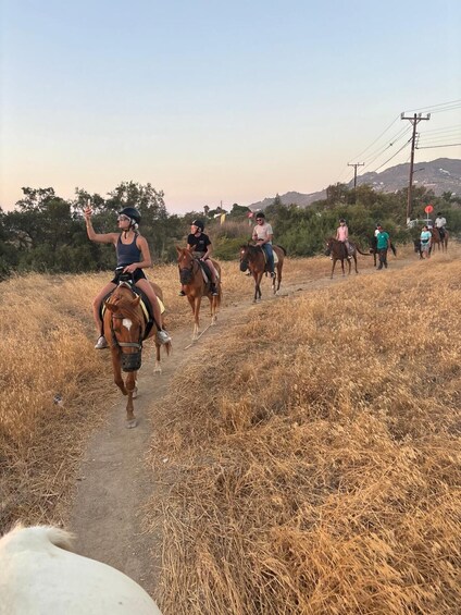 Un groupe de personnes à cheval, sur un sentier de terre, entouré d’herbes sèches et d’arbres. 2