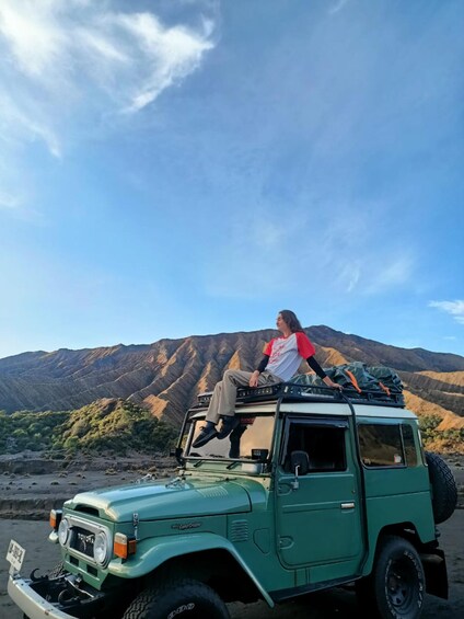 A person sitting on a green off-road vehicle with a mountainous landscape in the background. 4