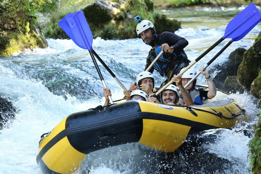 A group of people in a yellow and black raft navigating a river with rapids. 3