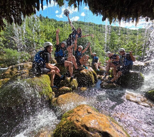 A group of people sitting on rocks by a waterfall in a forested area. 4