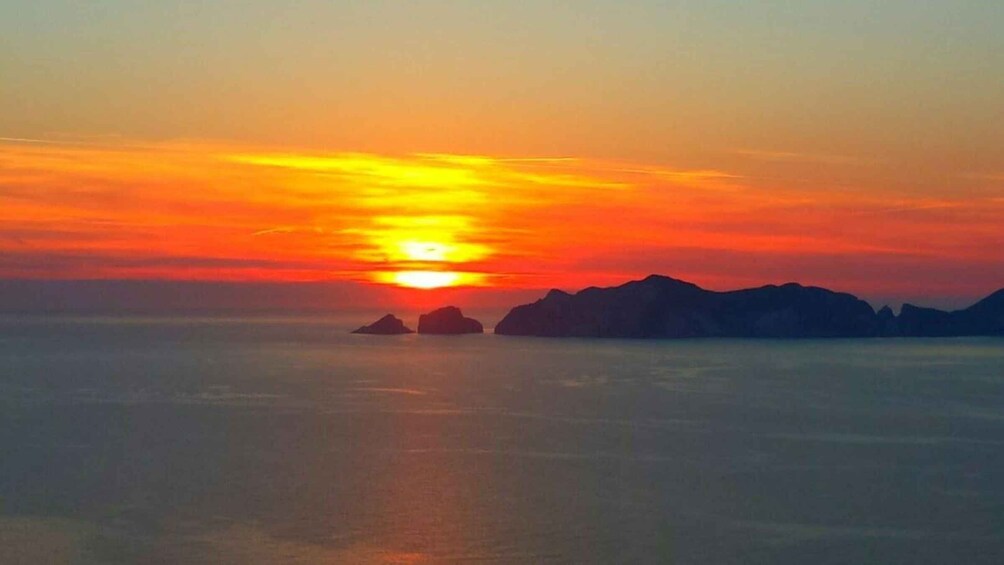 A sunset over a calm sea with distant rocky outcrops. 1