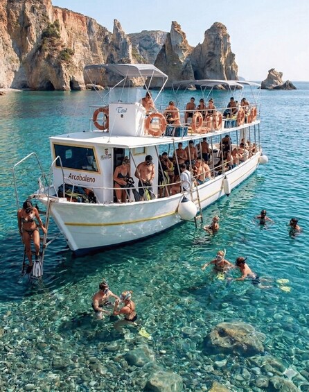 A boat named 'Arcobaleno' with people on board and others swimming in clear blue water near rocky cliffs. 2