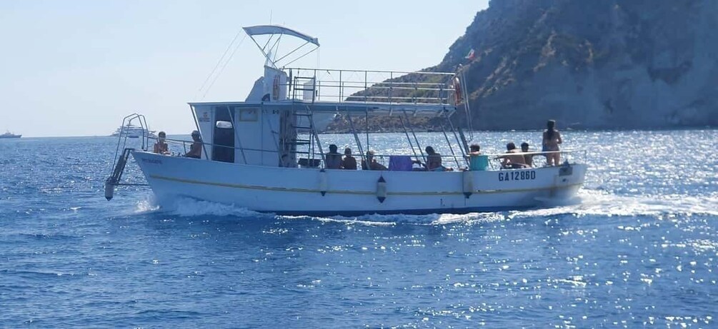 A white boat with people on board, moving through a body of water with a rocky coastline in the background. 5