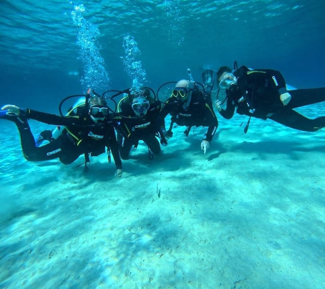 Four scuba divers underwater with fins and tanks, swimming in a clear blue ocean. 4