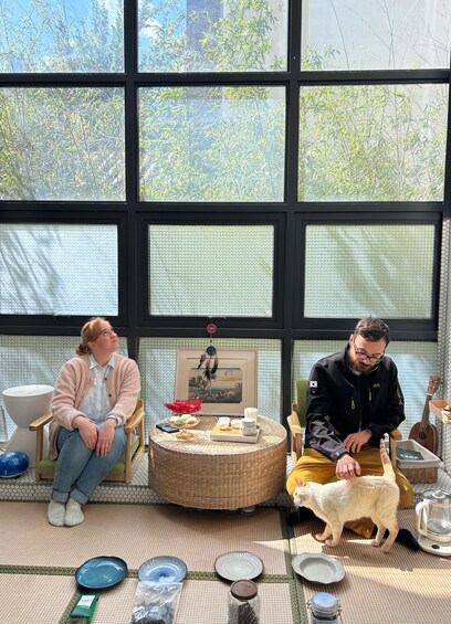 Two people sitting on chairs, a cat on the floor, and various items on a table. 3
