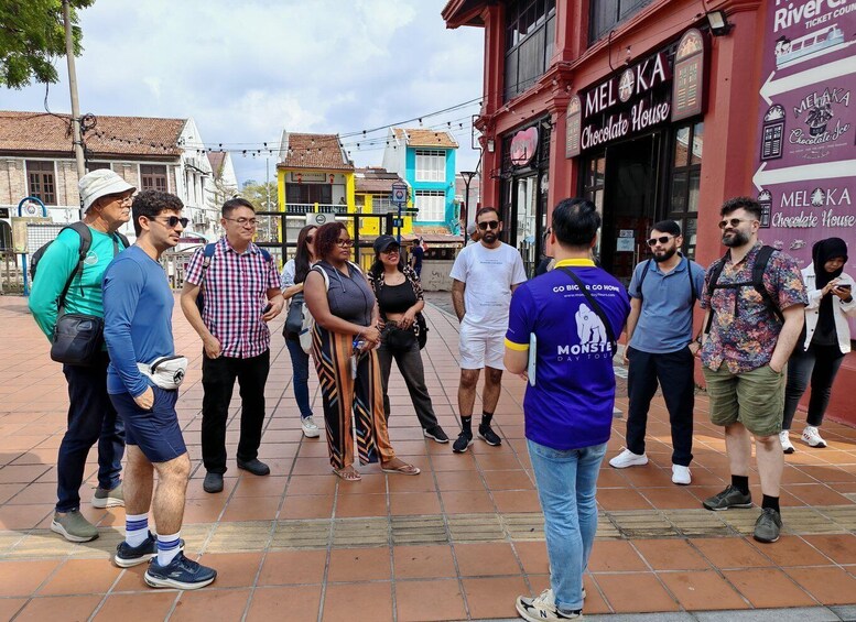 A group of people standing on a tiled street in front of a building with a sign that reads 'Melaka Chocolate House.' 1