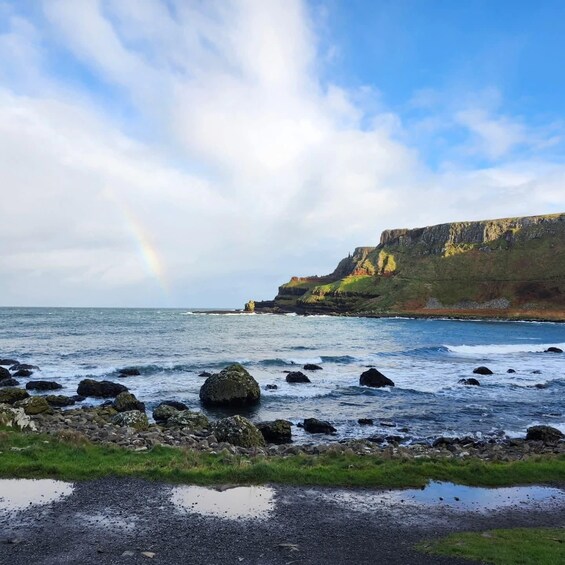 A coastal landscape with a rainbow, rocky shoreline, and cliffs. 5