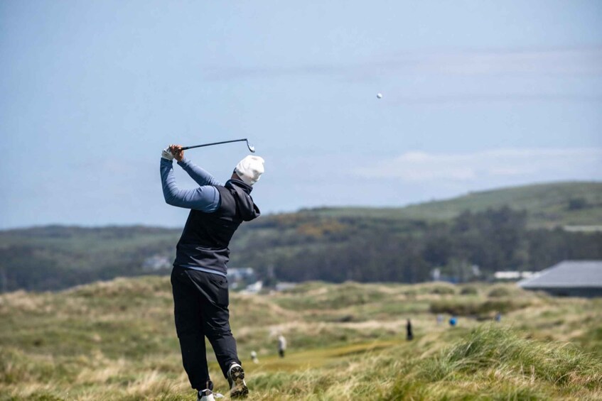 A person playing golf, swinging a club, with a clear sky and a hilly landscape in the background. 2