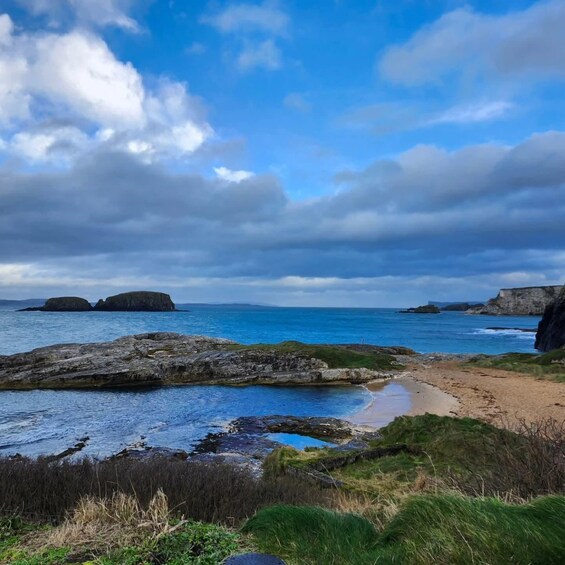 A coastal landscape with rocky outcrops, a sandy beach, and a clear blue sky. 1