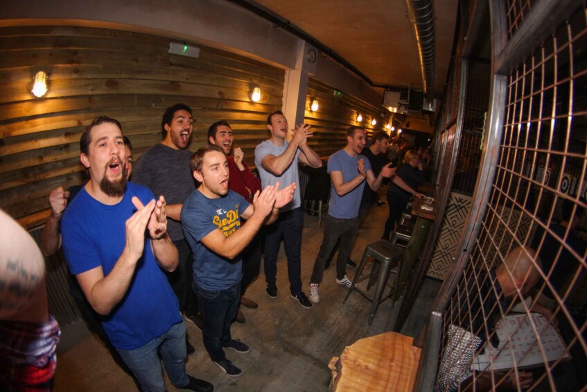 A group of people clapping in a dimly lit room with wooden walls and a metal fence. 5