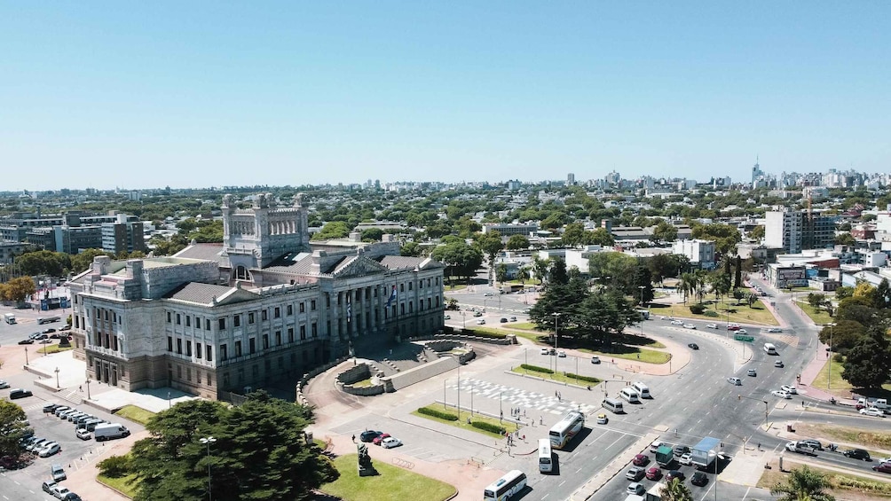 A cityscape with a prominent historical building, a roundabout, and a clear sky. 2