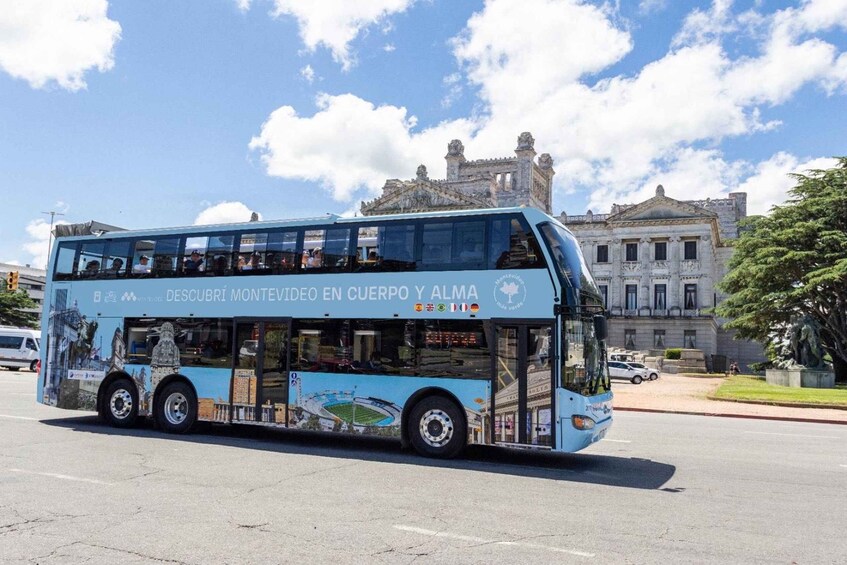 A double-decker bus with advertisements, driving on a road with a historic building in the background. 1