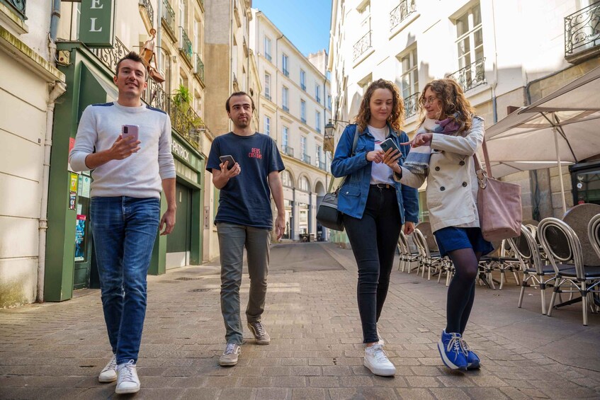 Four people walking on a cobblestone street in an urban setting with historic buildings and outdoor seating. 4