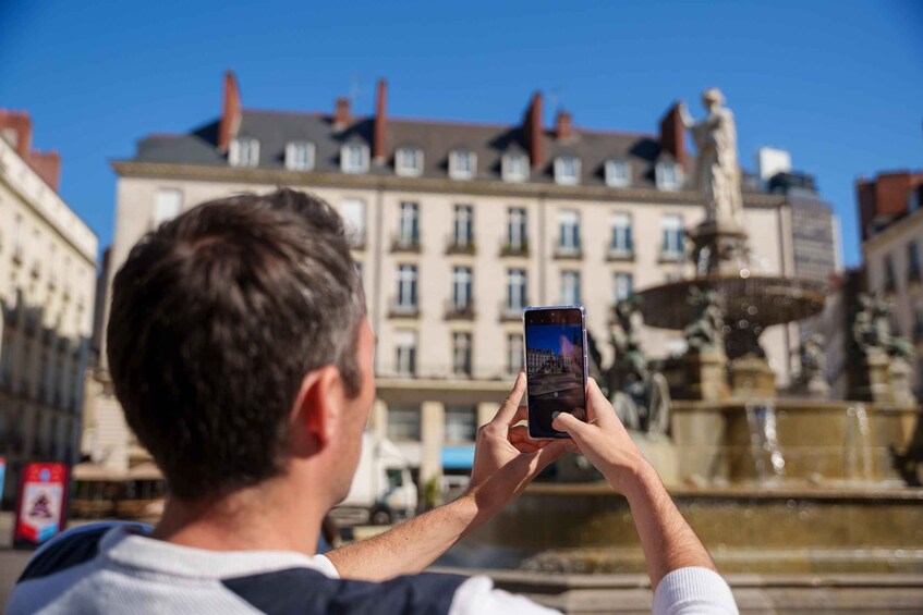 A person taking a photo with a smartphone of a fountain and buildings in the background. 2