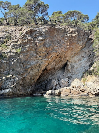 A rocky cliff with a cave entrance and turquoise water below. 5