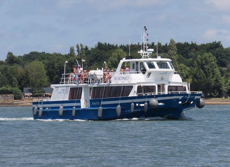 A blue and white boat named 'SUSCINIO' with passengers on board, moving on a body of water with trees and a stone wall in the background. 4