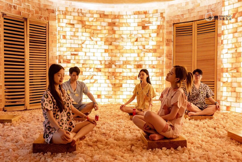 A group of people sitting on wooden platforms in a room with a brick wall and wooden shutters. 1