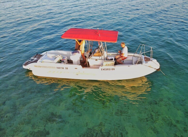 A white boat with a red canopy, labeled 'EXCURSION,' floating on clear blue water. 3